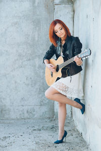 Portrait of woman playing guitar against wall