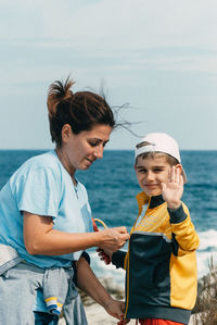 Mother and daughter standing at beach against sky