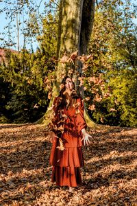 Woman throwing dry leaves while standing on land in forest