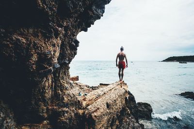 Man standing on rock by sea against sky