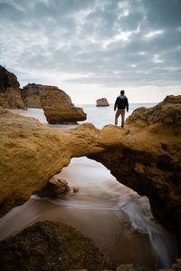 Rear view of man standing on rock formation at beach