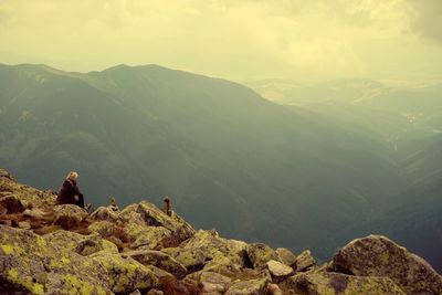 Rear view of people sitting on mountain against sky