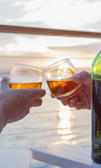 Cropped image of hands toasting against sea