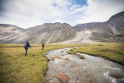 Two backpackers hike upstream of river to find safe crossing.