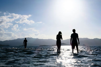 Silhouette people standing on sea against sky during sunset