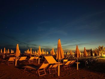 Lounge chairs and parasols on beach against sky during sunset