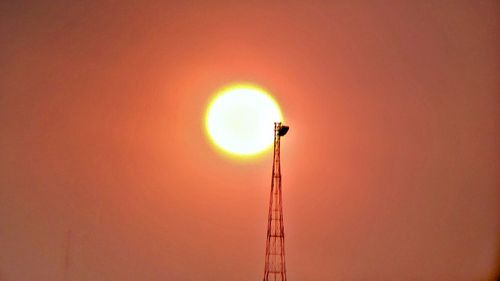 Low angle view of silhouette communications tower against orange sky