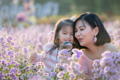 Cute girl looking through magnifying glass on flowering field with mother