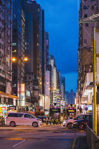 Cars on city street by buildings against sky at night