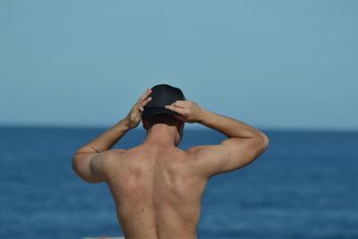 Rear view of shirtless man standing in sea against sky