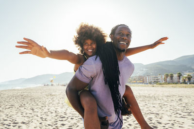 Smiling father piggybacking daughter with arms outstretched