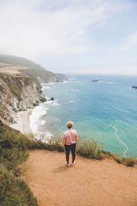 Full length rear view of man enjoying the view of sea and mountain cliff at big sur