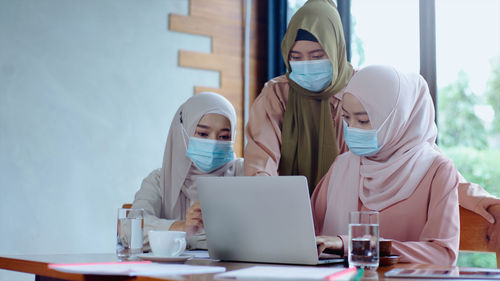 Businesswomen in hijab wearing mask looking at laptop in office