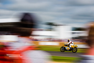 Rear view of spectator looking at racer riding motorcycle during racing