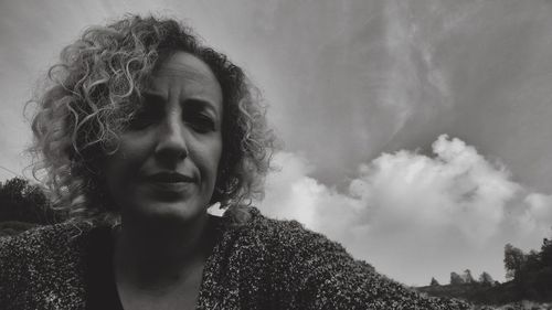 Portrait of woman with curly hair against cloudy sky