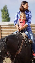 Happy woman riding horse with boy at ranch on sunny day