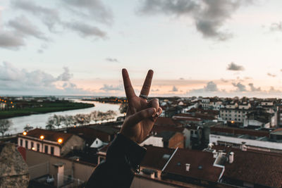 Cropped hand gesturing against sky during sunset