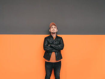 Portrait of young woman standing against orange background