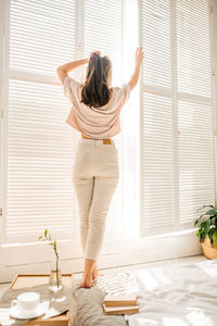 Rear view of woman standing by window at home