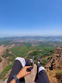 Low section of man on mountain against clear blue sky