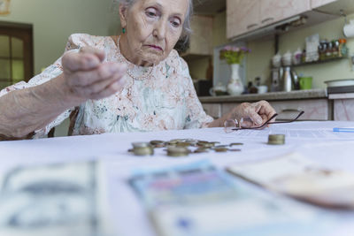 Confused senior woman looking at savings on table at home