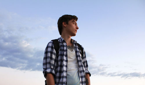 Low angle view of young man looking away while standing against sky