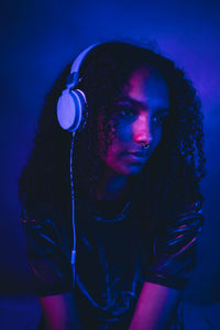 Beautiful woman with curly hair listening music through headphones in darkroom