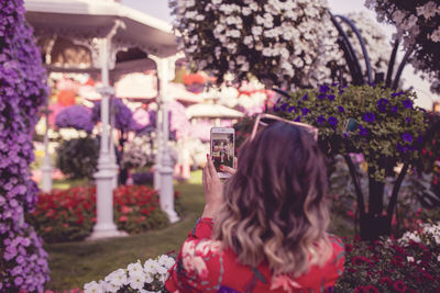 Rear view of woman photographing with mobile phone in public park