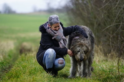 Smiling mature woman with dog on grassy field