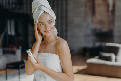 Smiling woman with perfume looking away while sitting at home