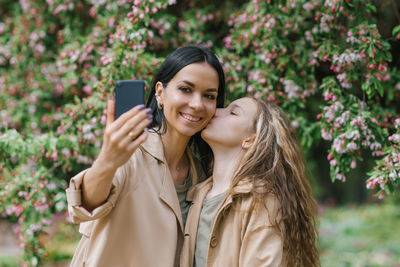 Happy family mom and her adorable teen daughter in the spring in the park selfie with a smartphone