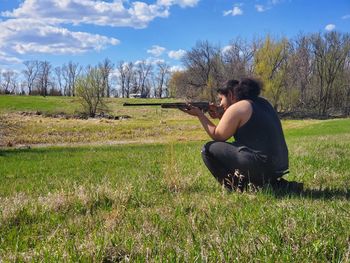 Side view of man kneeling in the country field with a rifle