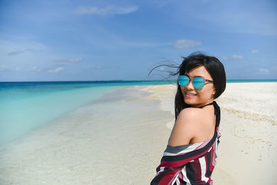 Young woman standing at beach against sky