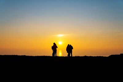 Silhouette people walking on landscape against orange sky