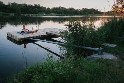 Woman resting on floating platform in lake during sunset