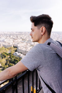 Man looking away while standing on railing in city