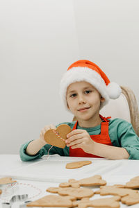 A cute boy in a santa hat holds a ginger cookie in the shape of a heart on a rope