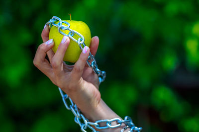 Cropped hand of woman holding granny smith apple with chain