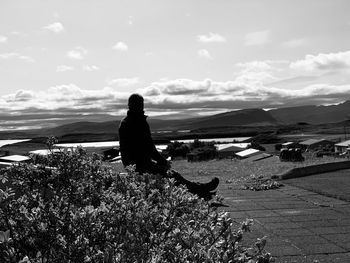 Rear view of woman sitting on mountain against sky