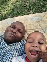 High angle portrait of smiling father and son lying on picnic blanket at park