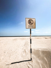 Information sign on sand at beach against sky
