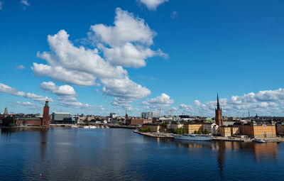 View of buildings by river against blue sky