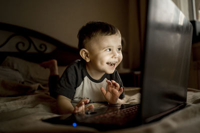 Happy boy with laptop lying on bed at home