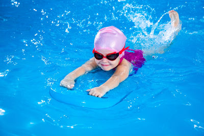 Preschool cute girl learning to swim in indoor pool with flutter board