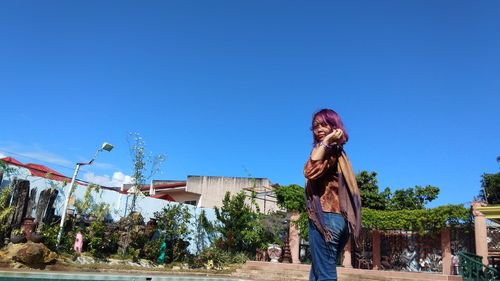 Portrait of woman standing against buildings and blue sky