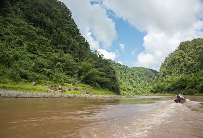 People motorboating on river in forest