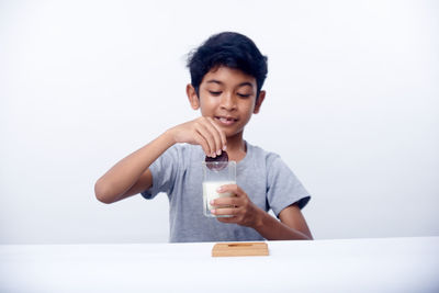 Young woman using mobile phone while sitting on table against white background