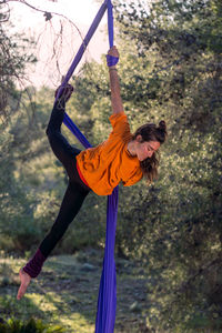 Young girl acrobat. practicing aerial silks. woman doing circus stunts with clothes in the forest. figured head position.