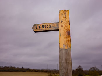 Low angle view of sign board on field against sky