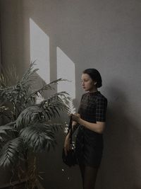 Young woman looking away while standing against wall